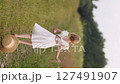 Young girl in white dress running along country road in summer field 127491907
