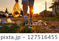 Young caucasian man cleaning street litter in urban setting at sunset, holding bag 127516455