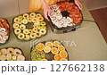 Hands arranging sliced apples, tomatoes, mushrooms, oranges, and kiwi on dehydrator trays 127662138