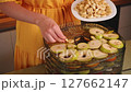 Housewife adding dried banana slices to a food dehydrator filled with various sliced fruits 127662147