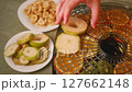 Woman carefully arranging pear slices onto a dehydrator tray, alongside other fruits like oranges and bananas, for healthy snack preparation 127662148
