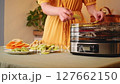 Housewife preparing a fruit dryer at home, filling it with various sliced fruits 127662150