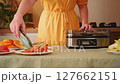 Housewife uses kitchen tongs to take jerky out of a food dehydrator 127662151