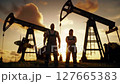 Proud Oil Field Workers Silhouetted at Sunset Wearing Overalls Under Golden Sky Standing in A Grassy Field 127665383