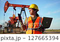 Woman in Yellow Hardhat With Laptop and Phone at Oil Rig in Bright Blue Sky 127665394