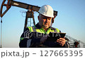 Worker in Hard Hat Using Tablet Near Oil Rig on Clear Sky Background 127665395