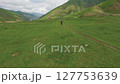 Cyclist riding narrow trail in mountain field 127753639