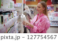 Woman choosing cosmetics in supermarket using phone scanner 127754567