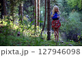 Blonde woman in short skirt stands in summer forest with arms crossed from cold 127946098