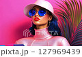 Fashionable woman cartoon character wearing sunglasses and hat holds a smartphone in front of a vibrant pink backdrop with tropical plants 127969439