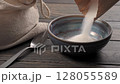 Pouring sugar into a bowl on a wooden table. 128055589