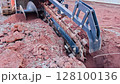 Trencher machinery is actively digging into earth at construction site 128100136