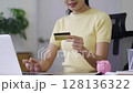 Young Woman Holding Credit Card While Using Laptop for Online Banking and Shopping at Home 128136322