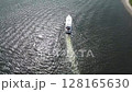 The boat glides across the tranquil blue water under a vast summer sky 128165630