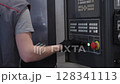 Factory worker operating a CNC machine control panel, adjusting settings during the machining process. Concept of automation, industrial control, manufacturing, and precision engineering 128341113