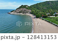 Drone flying over beachfront greenery and forested cliff 128413153