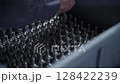 Close-up of a worker's hand carefully arranging uniform metal components inside a container. Concept of precision manufacturing, organization, and industrial craftsmanship 128422239