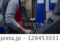 Worker operating CNC machine in industrial workshop, adjusting control panel and inspecting metal part. Concept of precision engineering, automation and modern manufacturing process 128453031