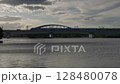 A sleek blue train crosses the Tamagawa River on a modern bridge as dramatic clouds fill the evening sky. Scenic urban railway footage capturing motion, architecture, and nature in harmony. 128480078