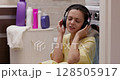 woman in headphones waits for the washing to finish and listens to music while sitting on the floor near the washing machine 128505917