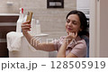 woman waits for the washing to finish and making selfie while sitting on the floor near the washing machine 128505919