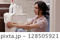 woman waits for the washing to finish while sitting on the floor near the washing machine in bathroom 128505921