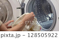 woman with basket doing laundry at home, female hand loading white laundry into washing machine. close-up 128505922
