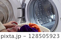 woman with basket doing laundry at home, female hand loading colour laundry into the drum of a home washing machine. close-up 128505923