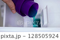 female hand pours liquid laundry detergent into compartment of washing machine, close-up 128505924