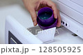 Woman pours liquid laundry detergent into compartment of washing machine, close-up 128505925