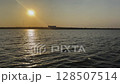 A wide expanse of water with gentle waves under an orange yellow sunset sky, with a distant shore on the horizon. Ukraine 128507514