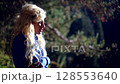 Sad blonde woman in blue standing in forest at sunset holding back tears 128553640