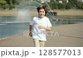 A Young Boy Joyfully Running by a Serene and Beautiful Lake Surrounded by Fountains 128577013