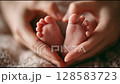 A close-up of gentle adult hands forming a heart shape around the tiny feet of a newborn baby, symbolizing love, care, and the precious bond between parent and child in soft natural light. 128583723