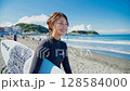 一位微笑的女子拿著衝浪板在藍天白雲的沙灘上散步 128584000
