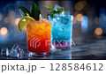 Vibrant, refreshing cocktails served on a marble table. One drink glows orange with lemon and leaves, the other shines blue with mint, both topped with ice. Perfect for a summer celebration. 128584612