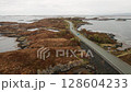 Atlantic ocean road reveals narrow track winding across rocky islands creating dramatic connection across sea. Norwegian landscape under overcast sky 128604233