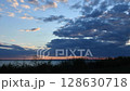 Transition of day to night as clouds drift across expansive sky during sunset over serene lake water. Colors shift dramatically, illuminating the horizon. 128630718
