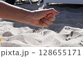 Woman hand pouring sand grains and then straighten and spread fingers of hand palm. Female hand playing with sand at sea beach in sunny summer day 128655171