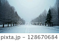 Peaceful winter landscape with a snow-covered road and frost-covered trees on a foggy day. Serene and cold atmospheric scenery.. 128670684