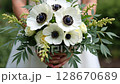 Woman holding a bouquet of white anemone flowers with green leaves. Elegant floral arrangement for weddings, celebrations, or spring events.. 128670689