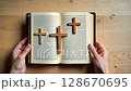 Three wooden crosses on an open Holy Bible held by hands. Concept of Christian faith, Easter, and the crucifixion of Jesus Christ. Top view. 128670695