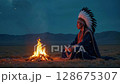 Native American tribal chief in a traditional feathered headdress sits motionless by the campfire at dusk, surrounded by rising smoke and flying embers under the open sky 128675307