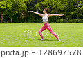 A woman doing yoga and pilates in a resort atmosphere under natural grass and blue skies 128697578