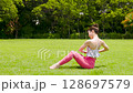 A woman doing yoga and pilates in a resort atmosphere under natural grass and blue skies 128697579