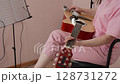 Side view of female guitarist cleaning her preferred acoustic guitar with dry tissue before beginning classical guitar lessons in home studio. Woman wearing pink polo shirt, jeans. Closeup, handheld 128731272