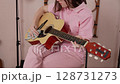 Young woman guitarist cleans her preferred acoustic guitar with dry cloth prior to commencing classical guitar lessons in home studio. Woman dressed in pink polo shirt, jeans. Close-up, handheld shot 128731273