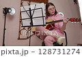 Young woman strums way to success as classical guitarist. She plays six string acoustic guitar with strumming style. Female guitar player is honing craft in home studio. Low angle view, handheld shot 128731274