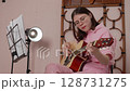 Woman guitarist is performing strumming style of Spanish guitar, utilizing six string acoustic instrument. Performance is taking place in musician's home studio in session of practice. Handheld shot 128731275