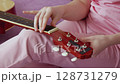 Closeup view of woman's hands tuning six string acoustic guitar. Hand moves methodically, tightening and loosening strings before playing. Guitarist unrecognizable, sitting on sofa in home. Handheld 128731279
